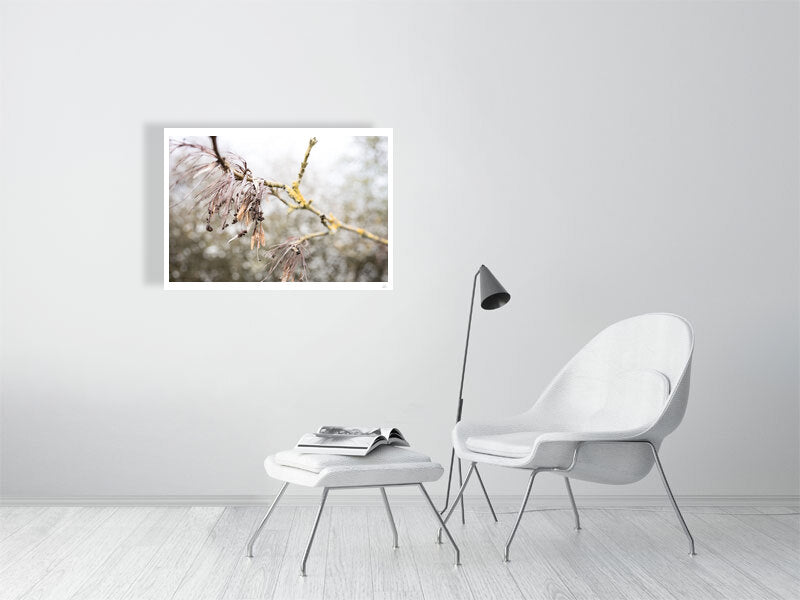 A1 print of winter's end displayed on a white wall, positioned behind and above a white living room chair. A white stool, intended for resting feet, sits nearby with a magazine/book atop it. Adjacent to the white chair stands a metal cone-shaped light fixture.