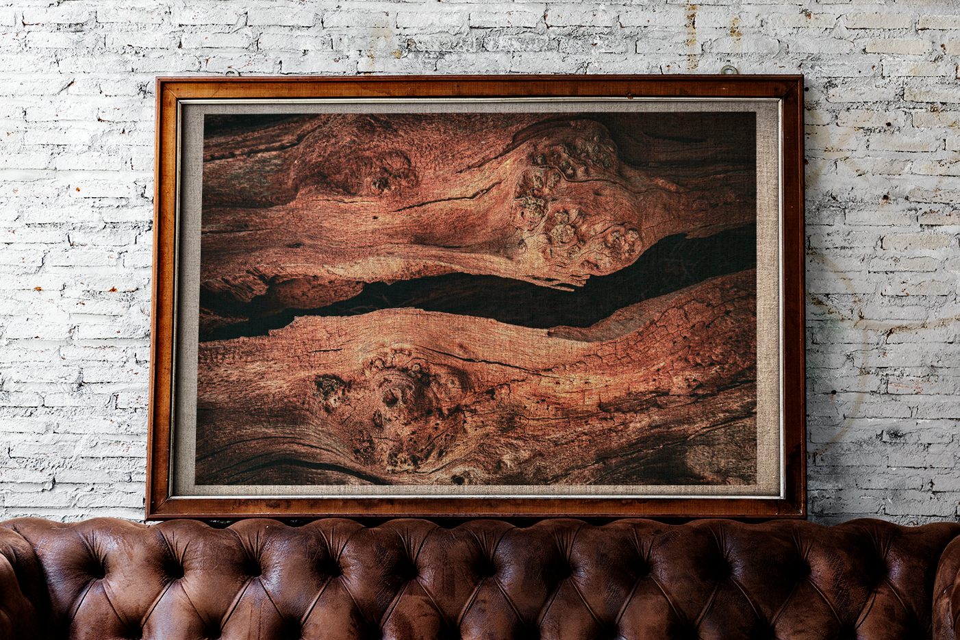 Split print in a brown frame, sitting on a leather studded sofa against a stone wall.