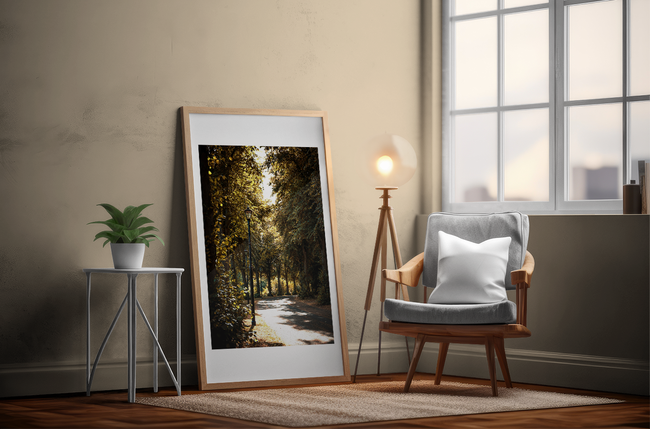 Autumn walks print laying against a wall next to some windows. lamps, chair and table with a plant site beside it. 