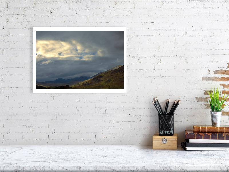 Snowdonia drama set in a minimalist office settings, pencil containter, books and a small plant. Place on a white painted brick wall.