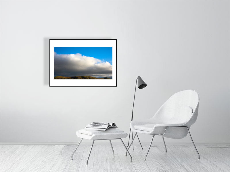 a1 with black frame Shire walks hung up in a white minimalistic living room. white chair, reading lamp, foot stall in view.