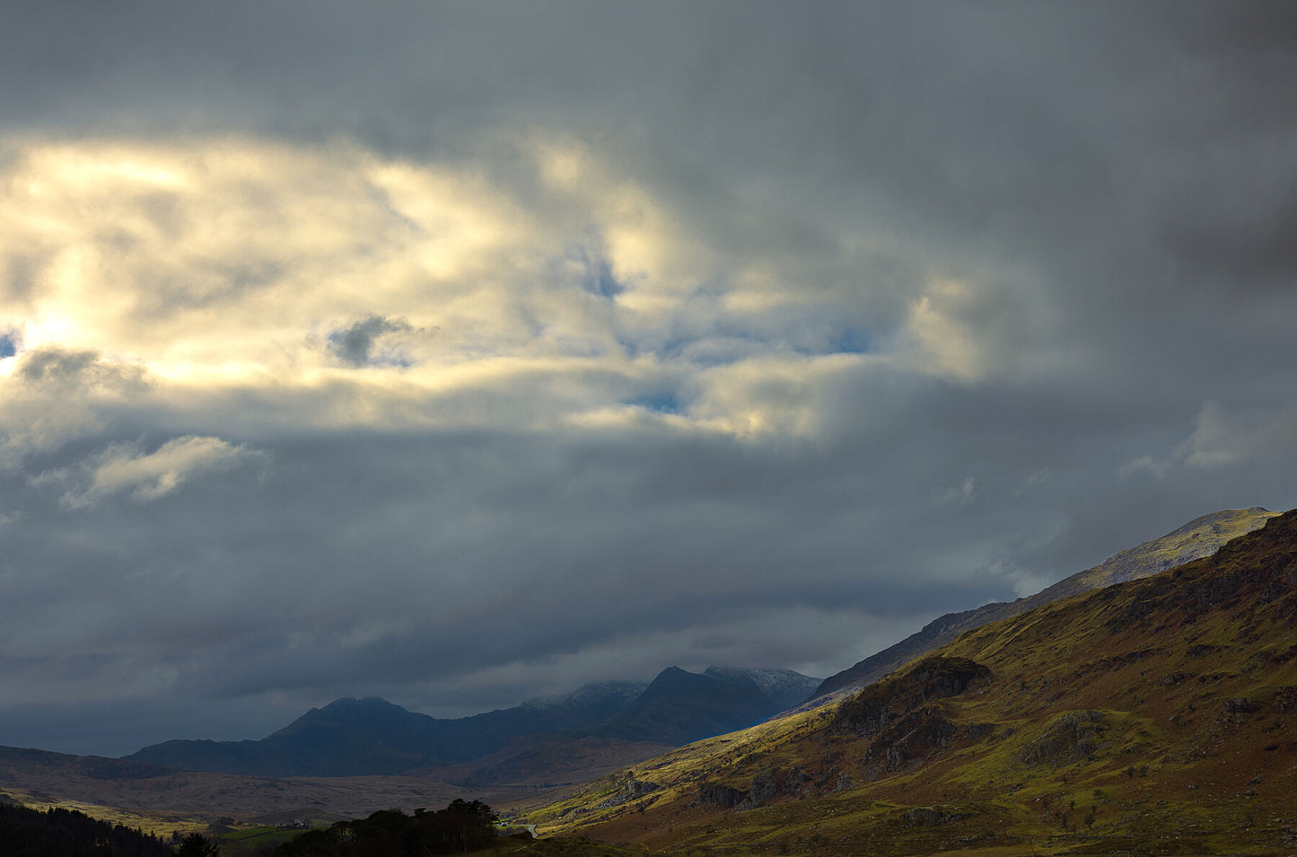 Overcast clouds, just parting allowing light to escape and hit the landscape. Snowdonia hills and mountains. 