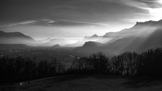 Dusk shot showing the last moments before the sun sets over the mountains. Light beams stream over them as a fog creeps up in the background over the city.